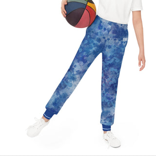Girl holding a colorful basketball wearing blue patterned pants and a white shirt on a white background